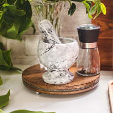 Lade das Bild in den Galerie-Viewer, Marble mortar and pestle on a wooden stand with a pepper grinder and plant in the background.