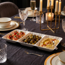 Load image into Gallery viewer, A white rectangular three-compartment serving tray filled with appetizers, set on a dark tablecloth in a dining environment with candles, glasses, and plates.
